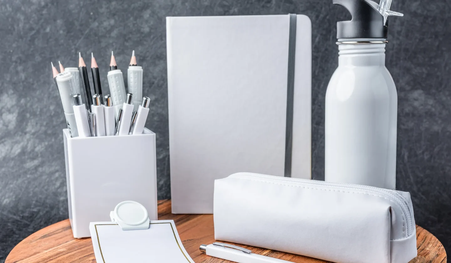 Zestaw białych gadżetów reklamowych bez nadruku ułożone na drewnianym stoliku